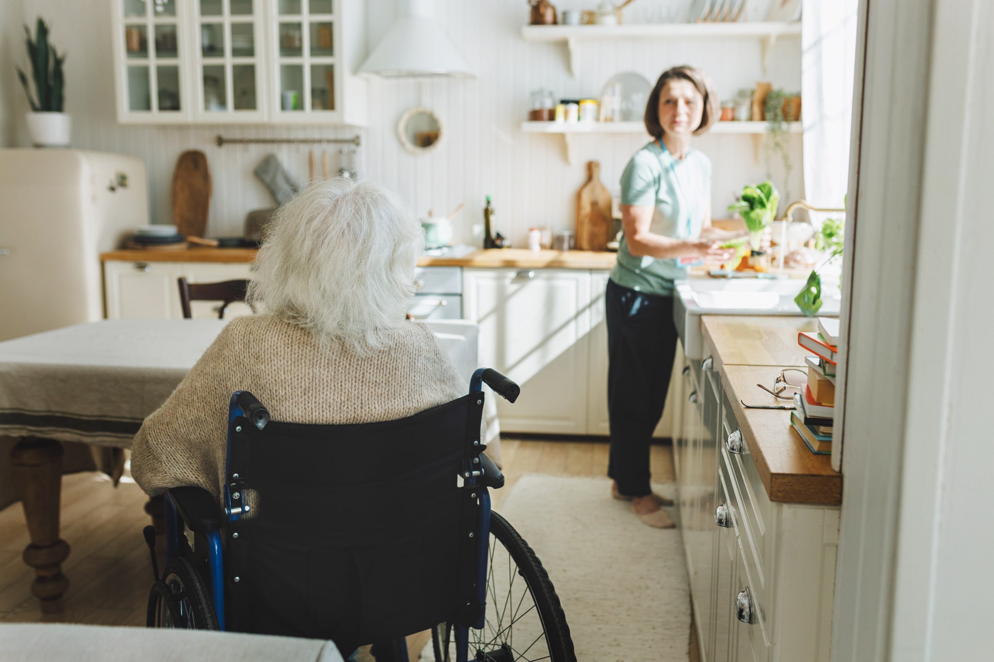 Caregiver preparing a meal in the kitchen while client watches from wheelchair